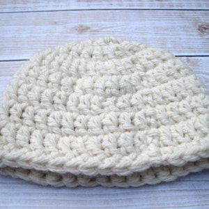 May include: A white crocheted beanie hat. The hat is made with a simple stitch pattern and has a folded brim.