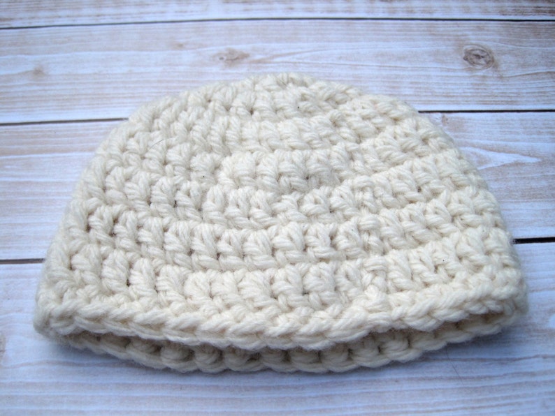May include: A white crocheted beanie hat. The hat is made with a simple stitch pattern and has a folded brim.