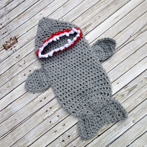 May include: Grey crocheted shark baby costume with a red and white mouth.