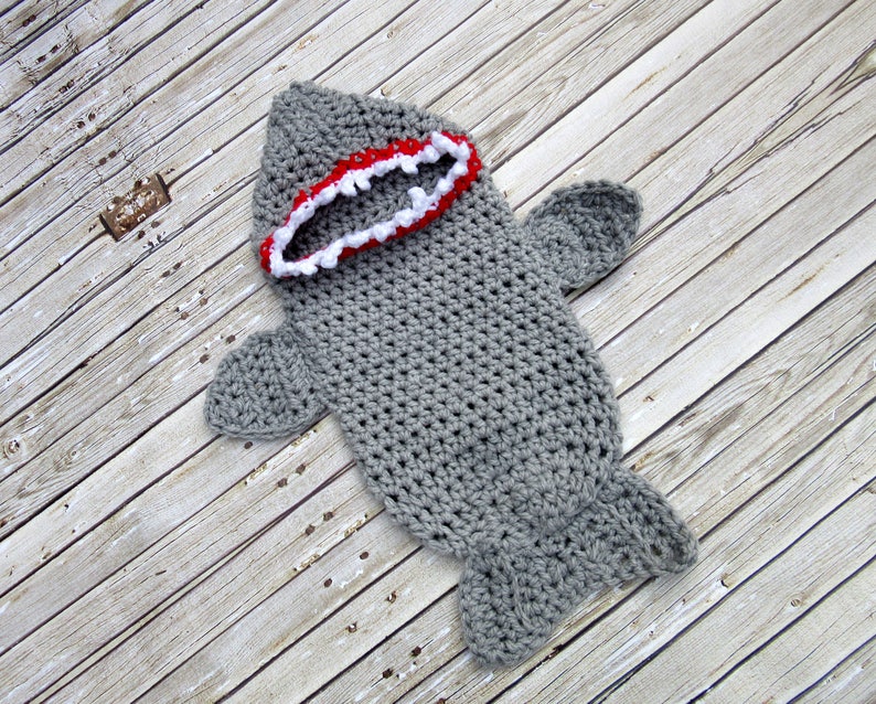 May include: Grey crocheted shark baby costume with a red and white mouth.