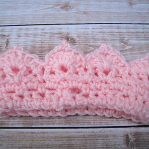 May include: A pink crocheted crown headband. The crown is made with a delicate open stitch pattern.