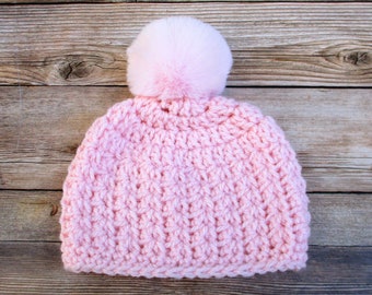 Könnte beinhalten: Eine rosa gestrickte Mütze mit einem flauschigen weißen Bommel oben.