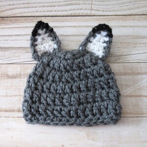 May include: Gray crocheted baby hat with white and black ears. The hat is made with a textured stitch.
