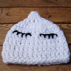 May include: A white, crocheted baby hat with black eyelashes. The hat is handmade and has a textured appearance. The hat is designed to fit a baby's head and is a soft, comfortable accessory.