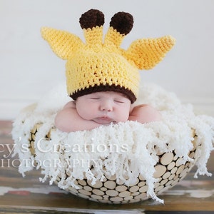 May include: A newborn baby wearing a yellow and brown crocheted giraffe hat, sleeping in a white, fluffy, round, woven basket.