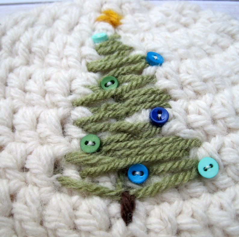 May include: A white crocheted hat with a green yarn Christmas tree design. The tree is decorated with colorful buttons.