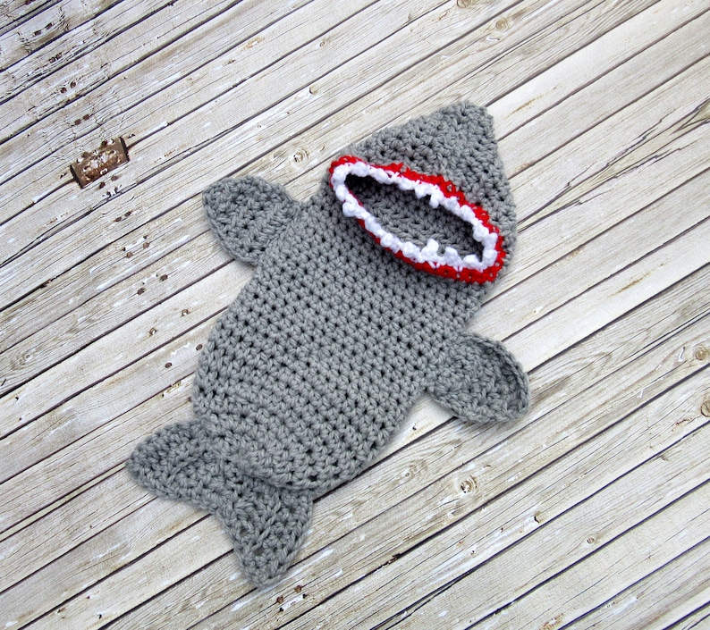 May include: Grey crocheted shark baby costume with a red and white open mouth.