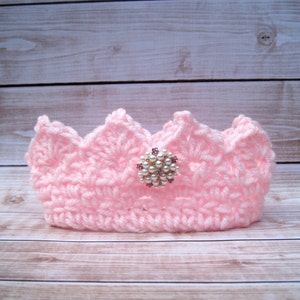 May include: A pink crocheted crown with a pearl and rhinestone embellishment.