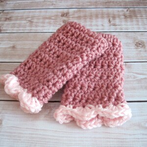 May include: A pair of pink crocheted fingerless gloves with a white crocheted trim. The gloves are made with a textured stitch and have a scalloped edge.