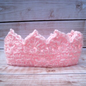 May include: A pink crocheted crown with a pointed top and scalloped edges.