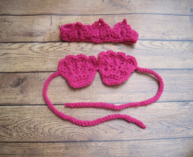 Op de afbeelding: Een fel magenta haakset bestaande uit een hoofdband met een geschulpte rand en een top met twee schelpvormige cups verbonden door een lang, dun gehaakt koord. Het garen heeft een getextureerd, gelust uiterlijk over het hele kledingstuk.