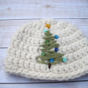 May include: A white crocheted beanie hat with a green felt Christmas tree design and colorful buttons.