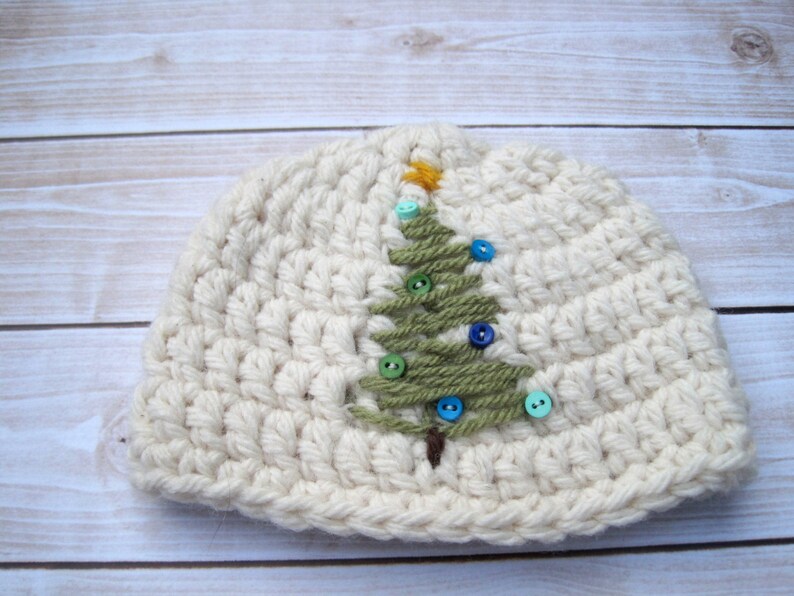 May include: A white crocheted beanie hat with a green felt Christmas tree design and colorful buttons.