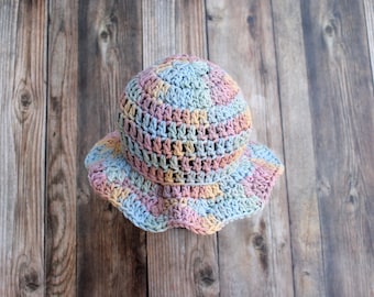 May include: A handmade crochet hat in pastel colors of blue, pink, and yellow. The hat has a rounded crown and a wide, ruffled brim. The hat is made of soft yarn and is suitable for warm weather.