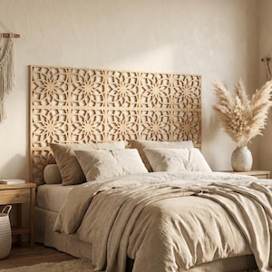 May include: A light-colored wooden headboard featuring a repeating laser-cut floral mandala pattern. The headboard is positioned behind a bed dressed in neutral-toned linens, including multiple pillows and a draped blanket in shades of beige.