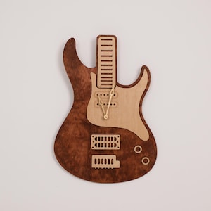 Può includere: Un orologio a forma di chitarra elettrica in legno con finitura in legno marrone e naturale. Il quadrante dell'orologio è sul corpo della chitarra e ha lancette dorate.