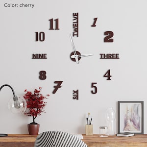 Könnte beinhalten: Moderne Wanduhr in Kirschfarbe mit einzelnen Zahlen und Wörtern. Die Uhrzeiger sind silberfarben und die Zahlen in einer serifenbetonten Schrift. Die Uhr ist an einer weißen Wand befestigt.