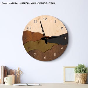 May include: A round wooden wall clock with a layered mountain design. The clock face features a natural wood color at the top, transitioning to shades of brown and black. The clock hands are black, and the numbers are carved into the wood.