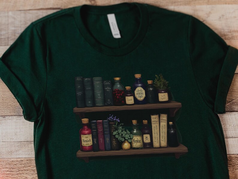 May include: A dark green t-shirt featuring a graphic print of two wooden shelves filled with various vintage books and glass apothecary bottles. The bottles have labels with text including Hemlock, Arsenic, and Morphine, alongside small plants.