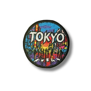 以下が含まれることがあります： 白い文字で「TOKYO」と書かれた丸い刺繍パッチ。パッチは、青と紫の空を背景に、歩行者と建物のあるカラフルなストリートシーンを描いています。黒い縁取りがあり、ジャケットやバッグに最適です。