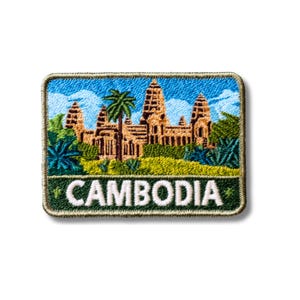 Może przedstawiać: Prostokątna haftowana naszywka przedstawiająca szczegółowy wizerunek kompleksu świątynnego Angkor Wat w Kambodży, otoczonego zielonymi palmami i roślinnością pod niebieskim niebem z białymi chmurami. Słowo CAMBODIA jest wyhaftowane na biało.
