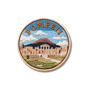 May include: A circular embroidered patch featuring a landscape of Pompeii with the text POMPEII arched at the top. The design includes a brown mountain, ancient stone ruins with columns, a green grassy foreground, and a blue sky with white clouds.