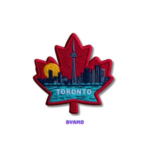 May include: Embroidered patch in the shape of a red maple leaf, featuring a Toronto skyline with the CN Tower, a yellow sun, and the word "TORONTO". The patch also includes the text "BYAMO".