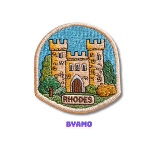Puede incluir: Parche bordado con una ilustración detallada de un castillo con el texto "RHODES" en la parte inferior. El parche tiene un fondo azul y un borde beige. La palabra "BYAMO" está escrita en morado debajo.
