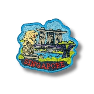 Op de afbeelding: Geborduurde patch met de skyline van Singapore, inclusief de Merlion en Marina Bay Sands. De patch heeft een blauwe rand en het woord "SINGAPORE" in het rood.