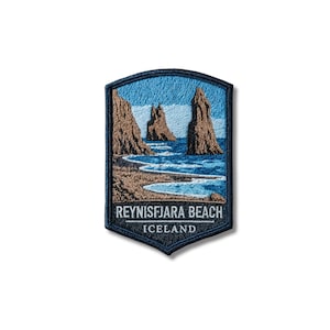 May include: A shield-shaped embroidered patch featuring a landscape of Reynisfjara Beach in Iceland. The design depicts brown rock formations, a dark sandy shoreline, and blue ocean waves. The text REYNISFJARA BEACH ICELAND is stitched in white.