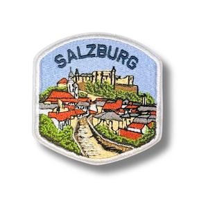 Könnte beinhalten: Ein sechseckiger gestickter Aufnäher mit einer Landschaft von Salzburg, einem Schloss auf einem Hügel, Gebäuden mit roten Dächern und grünen Bäumen. Das Wort SALZBURG ist in dunkelblauen Buchstaben oben vor einem hellblauen Himmel gestickt.