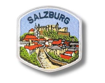 May include: A hexagonal embroidered patch featuring a landscape of Salzburg with a castle on a hill, red-roofed buildings, and green trees. The word SALZBURG is stitched in dark blue letters at the top against a light blue sky background.