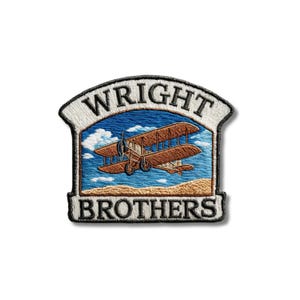 May include: An embroidered patch featuring a brown biplane flying over a tan landscape against a blue sky with white clouds. The word WRIGHT is stitched in black on a white arched top border, and BROTHERS is stitched in black on a white base.