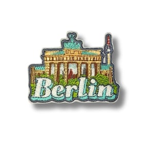 May include: Embroidered patch featuring a detailed depiction of Berlin landmarks, including the Brandenburg Gate and a tower. The patch is in shades of gold, green, and blue, with the city name "Berlin" in white script.