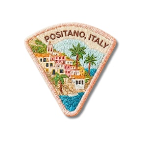 May include: A triangular embroidered patch featuring a coastal scene of Positano, Italy. The design includes colorful buildings, palm trees, and blue water, with the text POSITANO, ITALY stitched in brown thread along the top curved border.