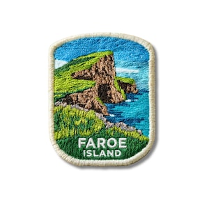 Op de afbeelding: Een rechthoekige geborduurde patch met afgeronde hoeken met een landschap van groene grasachtige kliffen die een blauwe oceaan ontmoeten. De tekst FAROE ISLAND is onderaan in wit garen geborduurd. De patch heeft een crèmekleurige rand.