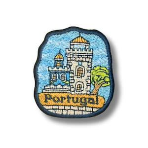 Puede incluir: Un parche bordado que muestra un castillo de piedra blanca con torres de tejados amarillos sobre un cielo azul claro. Un árbol verde se encuentra a la derecha del castillo. La palabra Portugal está bordada en letras azul oscuro sobre una banda beige.