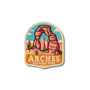 May include: An embroidered patch featuring a landscape of Arches National Park with a prominent red rock arch, blue sky, and green trees. The text ARCHES NATIONAL PARK is stitched in white letters on an orange background at the bottom of the patch.
