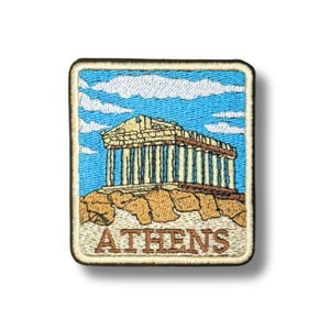 Può includere: Una toppa ricamata rettangolare raffigurante il Partenone di Atene, in Grecia. Il disegno mostra il tempio color marrone chiaro su una collina rocciosa contro un cielo azzurro brillante con nuvole bianche. La parola ATHENS è ricamata in marrone.