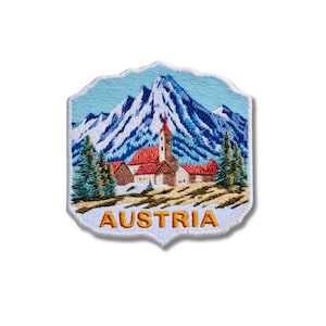 May include: An embroidered patch featuring a scenic landscape with snow-capped blue mountains, green pine trees, and a cluster of buildings with red roofs. The word AUSTRIA is stitched in yellow capital letters at the bottom of the patch.