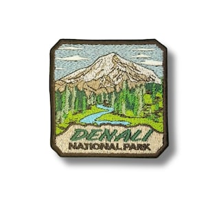 Könnte beinhalten: Gestickter Aufnäher mit einer Berglandschaft mit Fluss und immergrünen Bäumen. Der Aufnäher trägt den Text "DENALI NATIONAL PARK" in Grün und Braun. Der Aufnäher ist rechteckig mit einem braunen Rand.