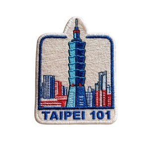 Può includere: Una toppa ricamata raffigurante il grattacielo Taipei 101 in tonalità di blu, centrata su uno sfondo color crema. Il design include uno skyline urbano stilizzato in rosso e blu, con la scritta TAIPEI 101 ricamata in blu nella parte inferiore.