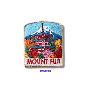Peut inclure: Écusson brodé représentant le Mont Fuji et une pagode. L'écusson a un fond de ciel bleu avec une montagne enneigée. La pagode est rouge avec des accents bleus, entourée d'arbres colorés. Le texte "MOUNT FUJI" est affiché sous la pagode, avec "BYAMO" en dessous.