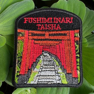 May include: Embroidered patch featuring a red torii gate, a traditional Japanese gateway, with the text "FUSHIMI INARI TAISHA" above it. The patch is black with green and white details.