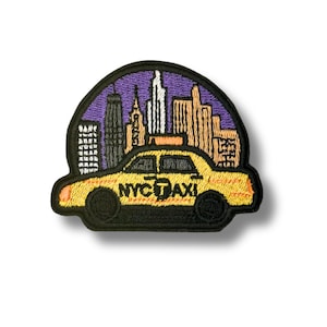 May include: An embroidered patch featuring a yellow taxi cab with the text NYC TAXI on the side. The background shows a stylized city skyline in shades of purple, tan, and white, all enclosed within a black border with a rounded top edge.