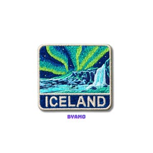 Pode incluir: Patch bordado com uma paisagem islandesa com uma cachoeira e a Aurora Boreal. O patch tem uma borda azul e a palavra "ICELAND" em branco. O texto "BYAMO" está abaixo da palavra "ICELAND".