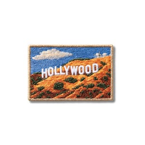 May include: A rectangular embroidered patch featuring the Hollywood sign in white lettering against a landscape of orange-brown hills and green shrubs under a blue sky with a single white cloud. The patch has a tan stitched border.