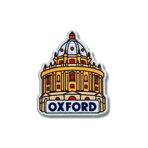 May include: An embroidered patch featuring a detailed depiction of the Radcliffe Camera building in Oxford. The design uses yellow, red, white, and blue thread, with the word OXFORD clearly stitched in bold blue capital letters at the base.