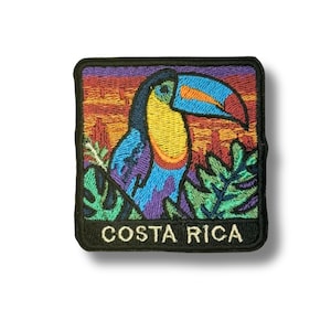 May include: Embroidered patch depicting a toucan bird with a blue beak, yellow chest, and purple and blue feathers, set against a sunset. The patch is square and has the words "COSTA RICA" in white.