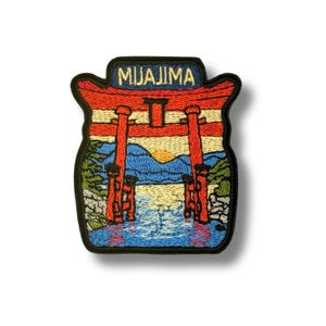 以下が含まれることがあります： 日本の宮島の象徴的な赤い鳥居を刺繍したパッチ。水、山、夕日を背景にしています。「MIYAJIMA」の文字が青いバナーで上部にあり、黒い縁取りがされています。